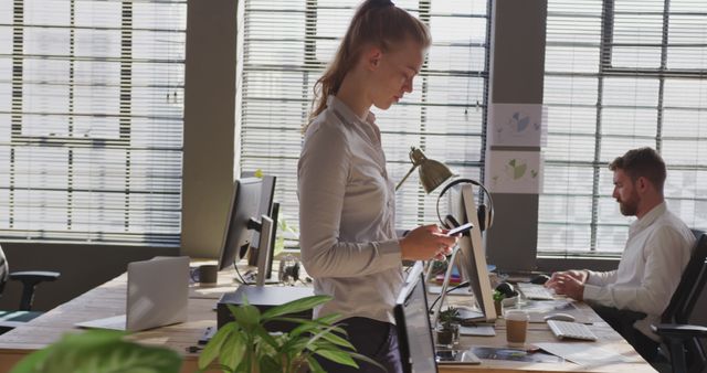 Businesswoman Using Smartphone in Modern Office with Colleague Working at Desk - Download Free Stock Images Pikwizard.com