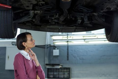 Professional female technician inspecting car undercarriage at service center