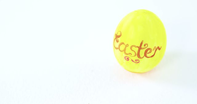A vibrant yellow Easter egg with the word Easter written on it stands out against a white background, with copy space. Its bright color and festive design evoke the joy and celebration associated with the Easter holiday.