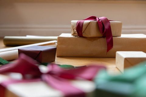 Kraft wrapped gifts sitting on light wood table with burgundy ribbon rustic holiday gifting scene