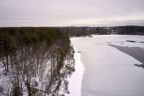 Drone view showing frozen lake and snow-covered forest lining winter shoreline