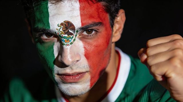 Intense mexican fan wearing tricolor face paint with national emblem, clenched fist
