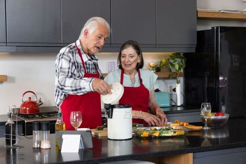 Senior Couple Operating Food Processor and Preparing Vegetables in Modern Kitchen