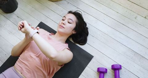 Asian woman relaxing on yoga mat using smartwatch outdoors