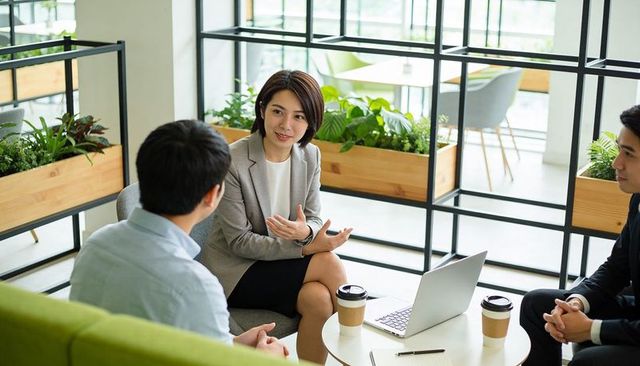 Businesswoman leading team discussion in modern green office lounge, collaborating