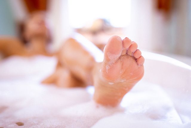 Foot of biracial woman taking bath, relaxing in foam. domestic lifestyle and self care, enjoying leisure time at home.