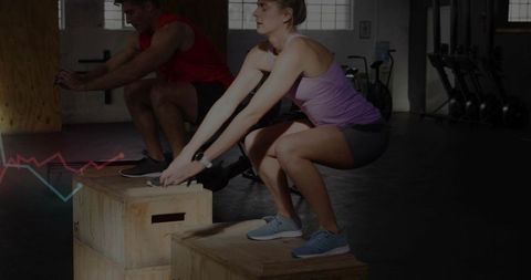 Partner plyometric box squat workout in industrial gym, woman in purple tank and man in red top