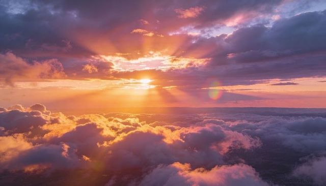 Sunrise above clouds with radiant sunbeams and pastel sky over aerial cloudscape