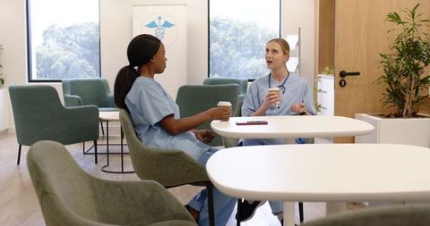 African american and caucasian nurses enjoying coffee break in modern clinic staff lounge