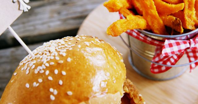 Perfect for food blogs, restaurant advertisements, menu designs, and culinary magazines. This image captures the mouth-watering detail of a freshly prepared burger with a sesame bun next to crispy sweet potato fries in a vintage metal bucket. Ideal for promoting fast food joints, recipe articles, or food truck events.