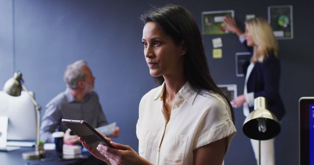 Focused Businesswoman Holding Tablet in Busy Office Environment - Download Free Stock Images Pikwizard.com