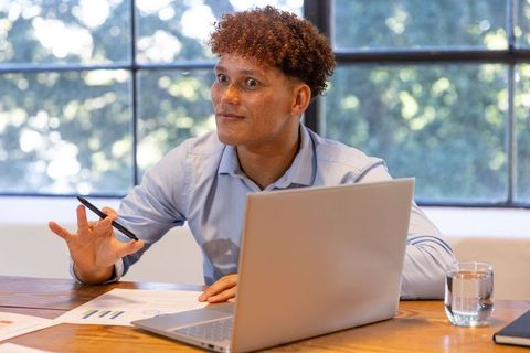 Young professional man gesturing during meeting with laptop and documents in bright office