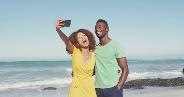 Smiling diverse couple taking selfies with smartphone on sunny beach by the sea. Summer, free time, relaxation, romance and vacations.