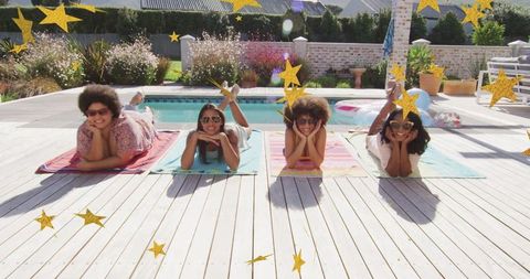 Four women sunbathing on colorful towels by backyard pool enjoying summer sunshine and relaxing