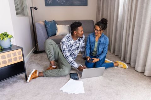 Young diverse couple reviewing bills and planning budget on laptop and phone in living room