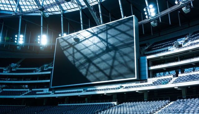 Stadium with suspended led scoreboard casting geometric shadow over tiered seating