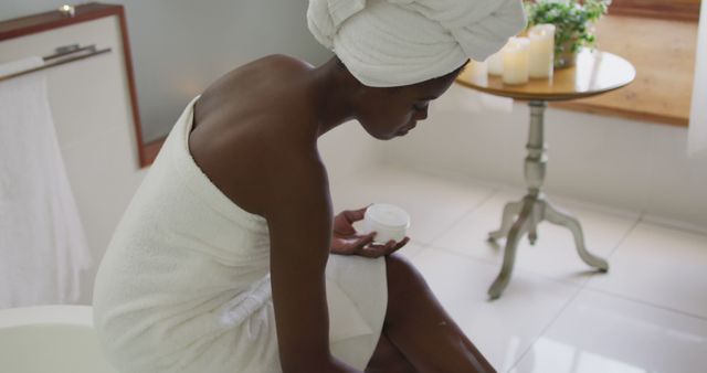 African american attractive woman applying body balm in bathroom. beauty, pampering, home spa and wellbeing concept.