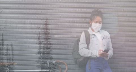 Woman with Mask Using Smartphone Amidst Winter Background