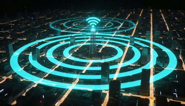 Telecom Tower Broadcasting WiFi Coverage Across Nighttime Urban Grid With Cyan Signal Rings