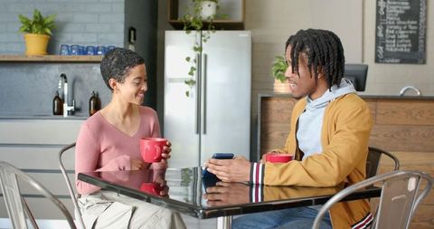 Diverse young adults sharing coffee and smartphone at modern kitchen cafe table