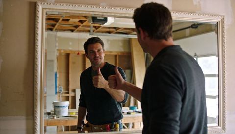 Handyman giving thumbs-up while inspecting mirror reflection during garage renovation