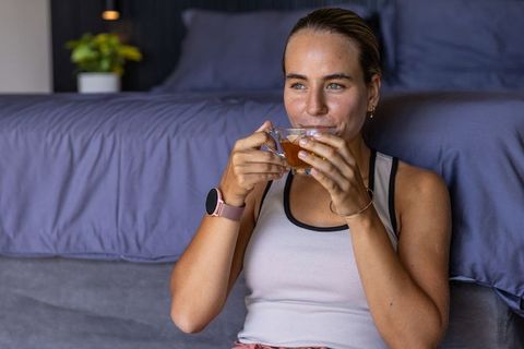 Young woman sipping tea on bedroom floor, enjoying calm morning relaxation and mindfulness