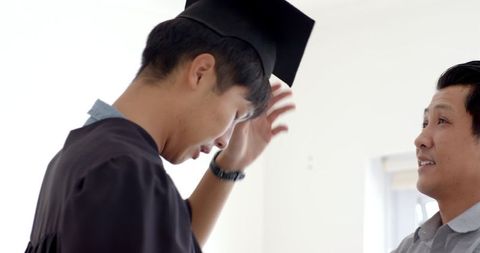 Young graduate smiling proudly with supportive father indoors