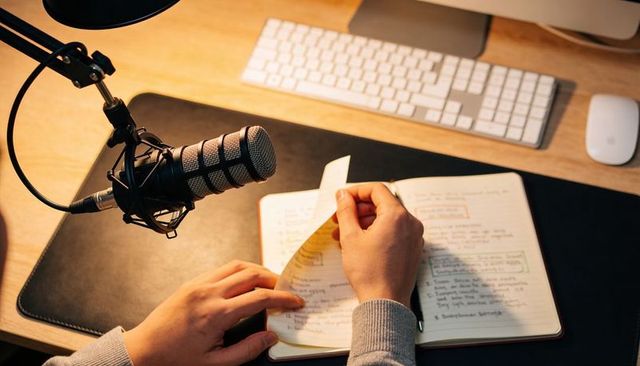Recording podcast from home desk with professional microphone and handwritten notes