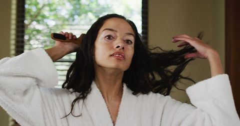 Biracial Woman Brushing Hair in White Robe at Home
