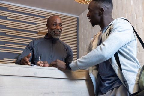 Smiling african american receptionist guiding young visitor signing check-in forms in modern lobby