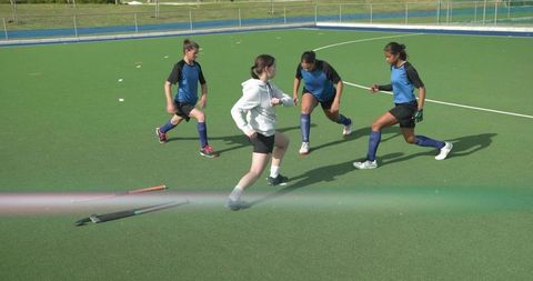 Teen girls field hockey players intercepting ball during school practice on green turf