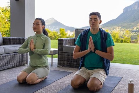 Couple practicing mindful yoga kneeling on patio mats with mountain view and tracker
