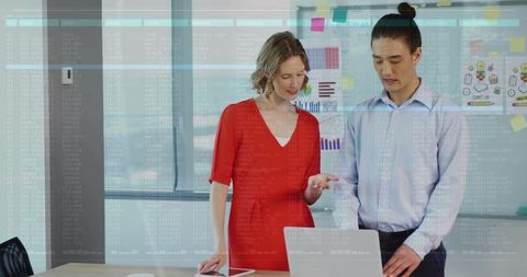 Business team collaborating over laptop and whiteboard with charts and sticky notes