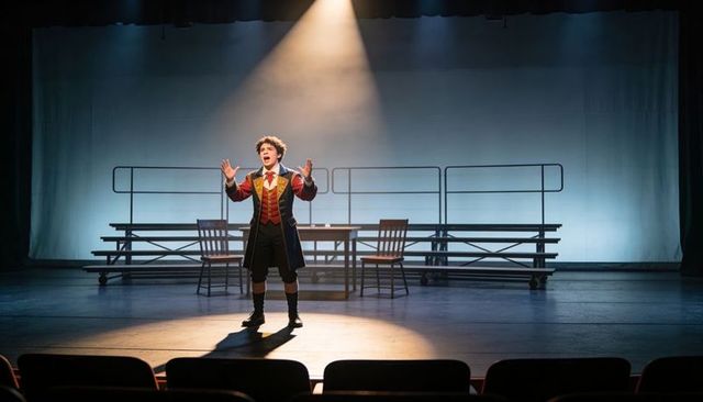 Young Male Actor Performing Monologue in Period Costume Under Spotlight on Empty Stage