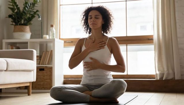 Woman practicing mindful breathing on yoga mat in sunlit living room for calm wellness