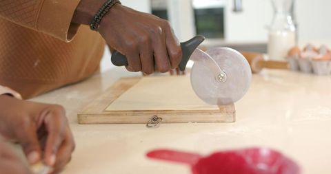 African american couple cutting rolled dough with pizza cutter on flour-dusted counter