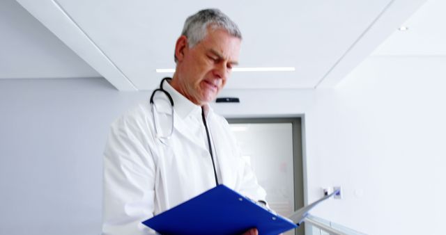 Senior Doctor Reviewing Medical File in Modern Hospital Corridor - Download Free Stock Images Pikwizard.com