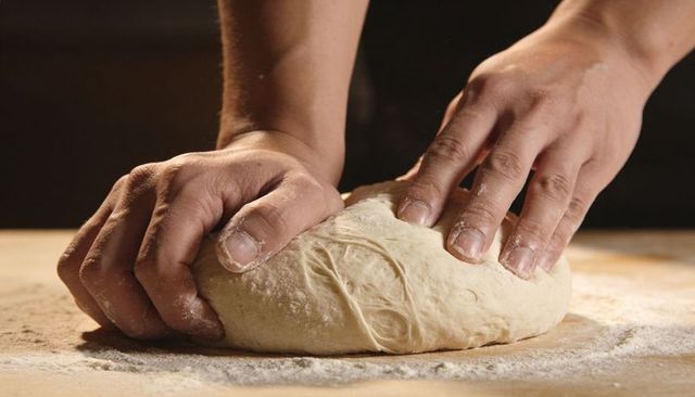 Hands Kneading Dough on Floured Wooden Board, Shaping Artisan Bread, Closeup Detail