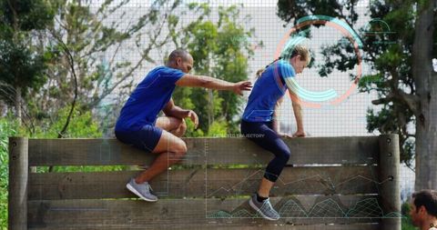Training partners scaling wooden barrier in forest