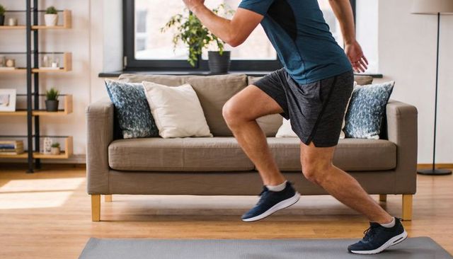 Man lunging during home workout on exercise mat in bright living room with greenery