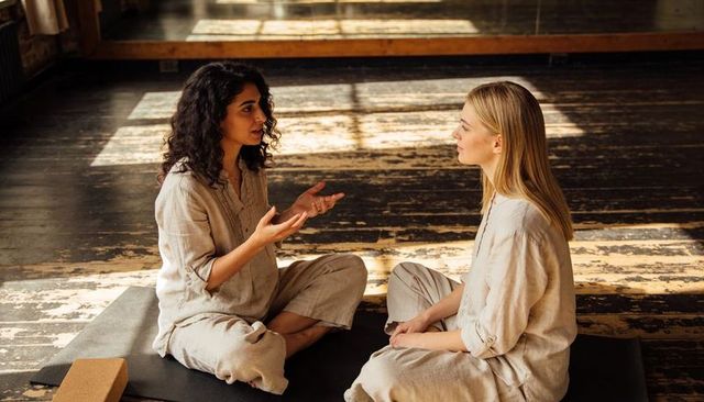 Two women practicing mindful dialogue on yoga mats in sunlit studio wearing linen