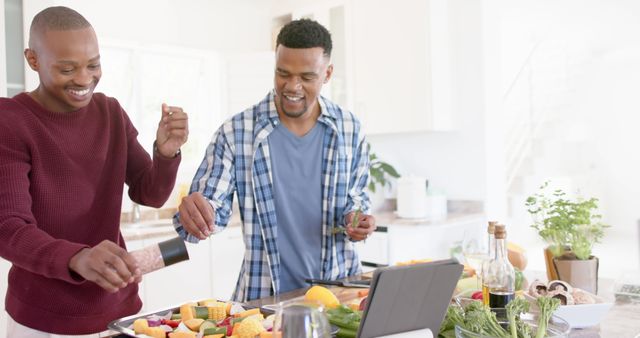 Happy diverse gay couple preparing meal, using laptop in kitchen at home. Togetherness, relationship, cooking, technology and domestic life, unaltered