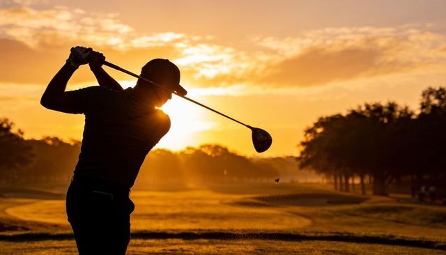 Silhouetted golfer swinging driver at sunrise on misty fairway with golden backlight