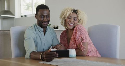 Couple Smiling While Watching Smartphone Together at Home