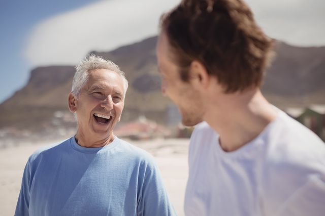 Cheerful senior man with his son standing at beach during sunny day
