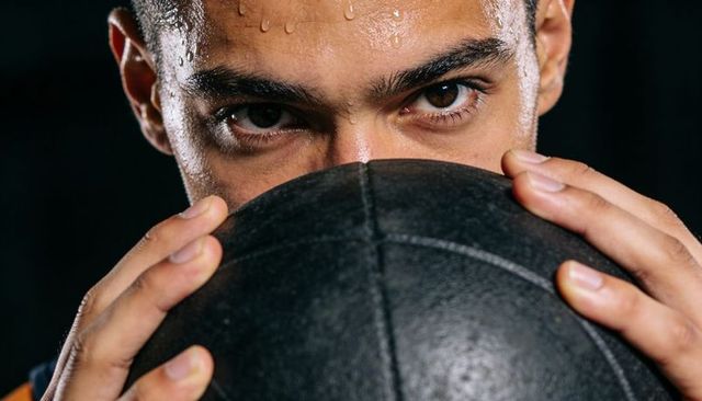 Intense athlete gripping black medicine ball, sweating and focusing during gym workout