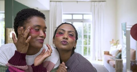 Female friends using red under-eye patches in cozy living room