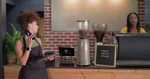 Barista calling orders while coworker preparing espresso at busy cafe counter with grinders