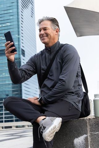 Middle-aged man checking smartphone during urban fitness break in dark activewear