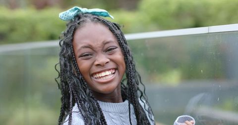 Laughing African American girl with braided hair and teal bow on outdoor balcony